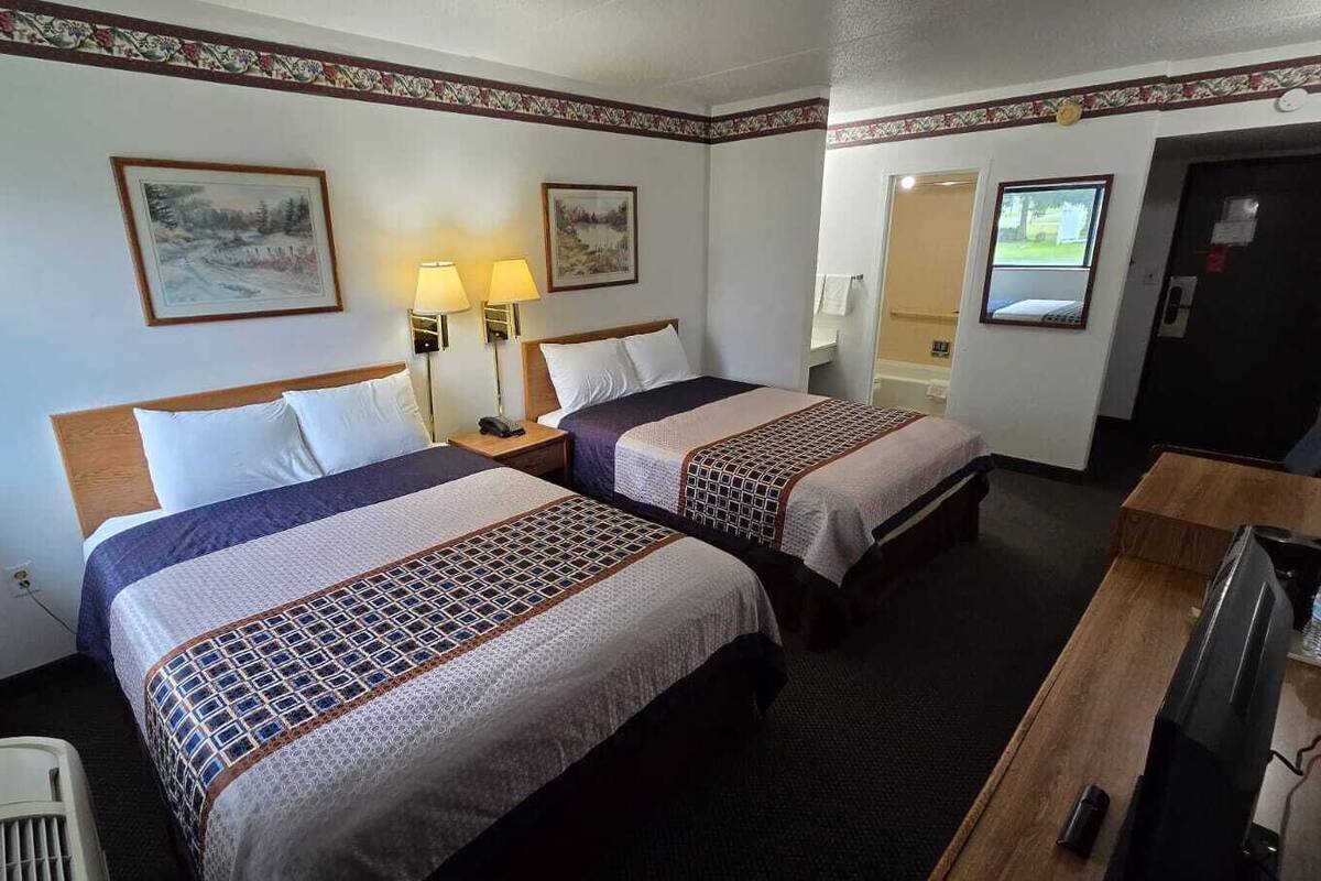A hotel room with two beds, a desk, a television, and two wall-mounted lamps.