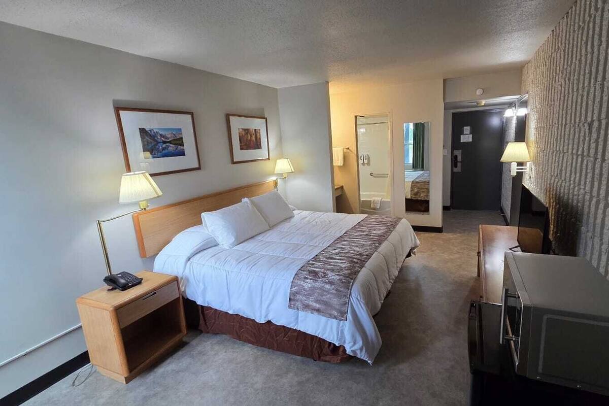 A hotel room with a bed, bedside lamps, a desk, and a television.