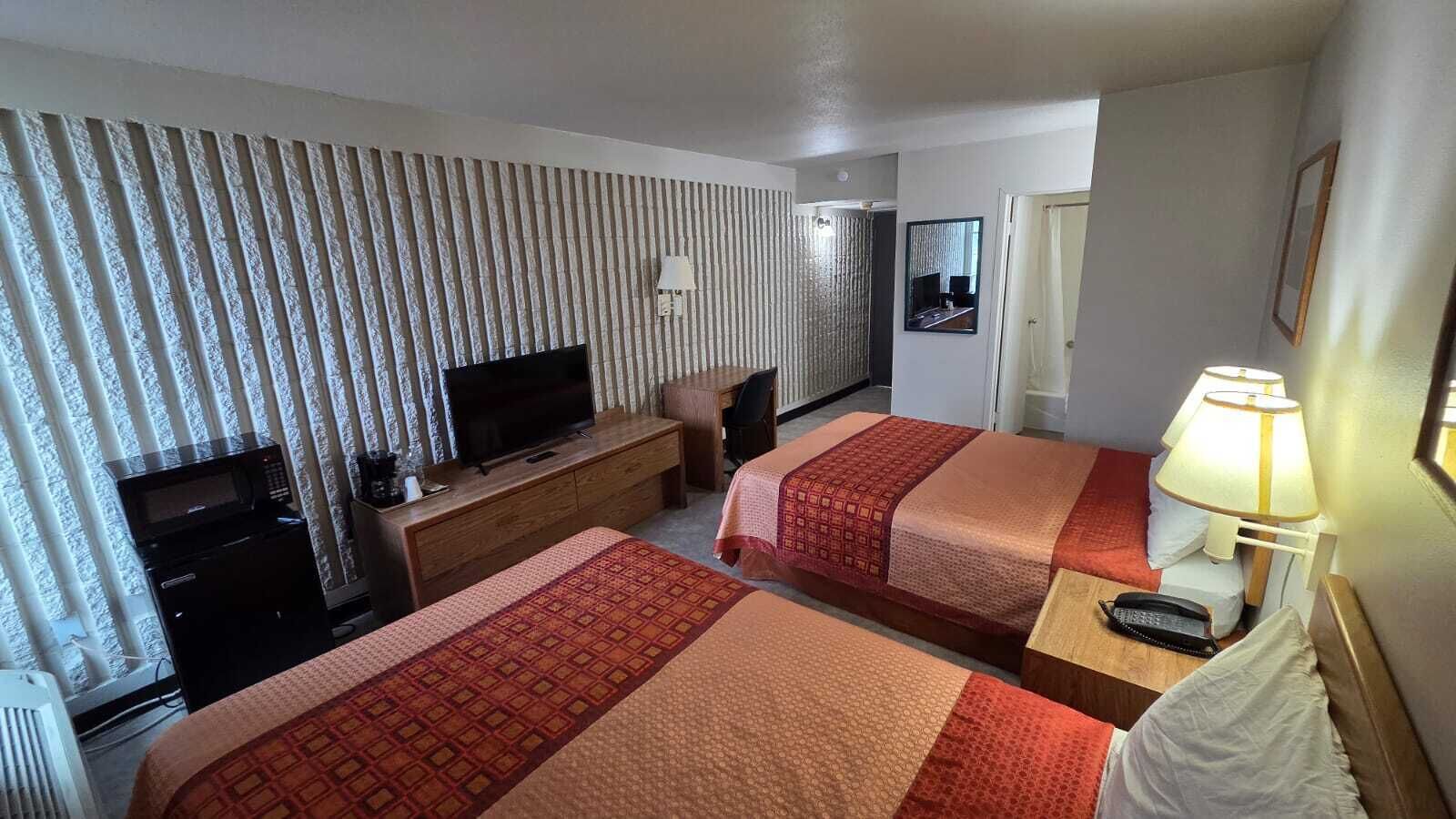 Habitación de hotel con dos camas, televisión, escritorio y microondas.