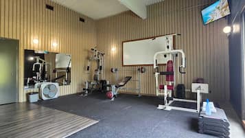 A gym with various exercise equipment, a large mirror, and a television on the wall.