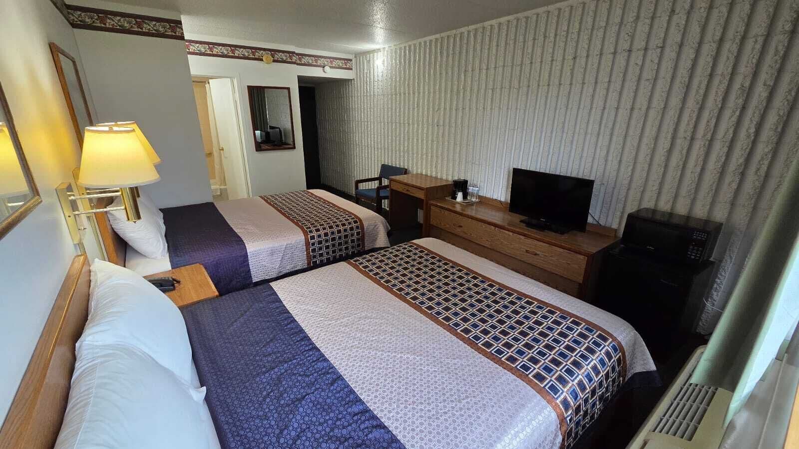 A hotel room with two beds, a desk, a television, and a mirror.