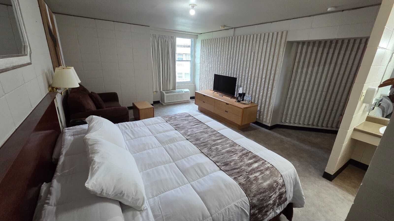 A hotel room with a large bed, a TV, a desk, and a window with curtains.