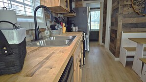 A modern kitchen with wooden countertops, stainless steel appliances, and a built-in dishwasher. - Redbud Roost Tiny Home (Big Cabin)