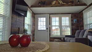 A dining area with a wooden table, two apples, and a woven placemat. - Redbud Roost Tiny Home (Big Cabin)