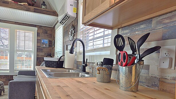A modern kitchen with a wooden countertop, a sink, and a window with blinds. - Redbud Roost Tiny Home (Big Cabin)