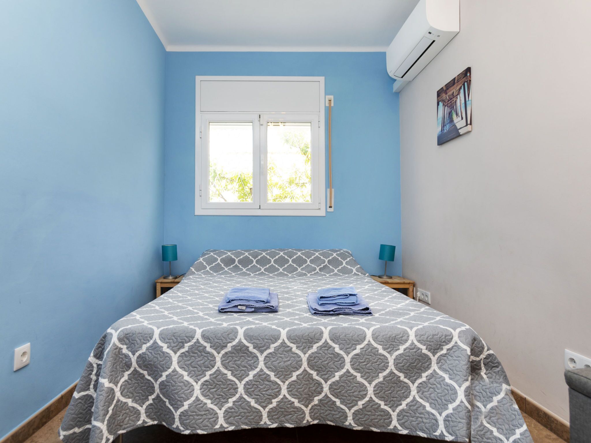 Een slaapkamer met een bed, twee nachtkastjes, een raam en een airconditioning.