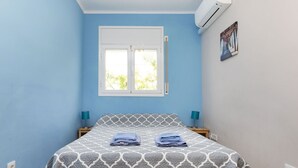 A bedroom with a bed, two bedside tables, a window, and an air conditioning unit. - Junqué-Verdure by Interhome (Miami Platja)