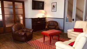 Een kamer met twee leren fauteuils, een witte bank, een rode tafel en een open haard.