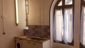 Een kleine keuken met een wasmachine, een spoelbak en een raam met gordijnen.