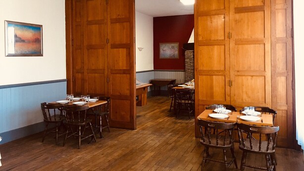 Un espace repas avec des tables et des chaises en bois, un ventilateur de plafond et un tableau accroché au mur.