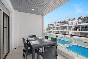 Un balcon avec une table dressée pour quatre personnes, donnant sur une piscine et un immeuble à plusieurs étages doté de balcons.
