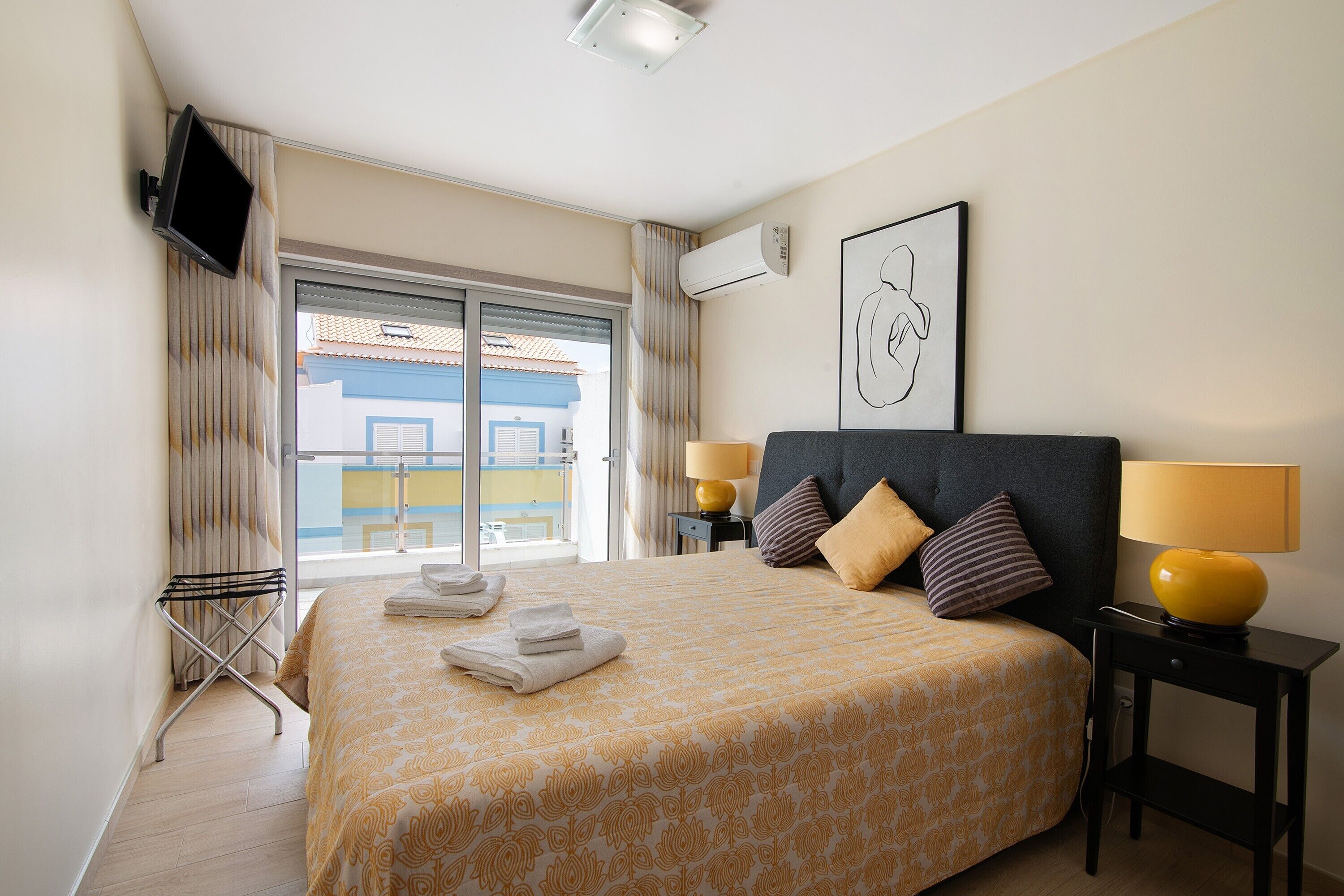 Habitación de hotel con cama, dos lámparas de noche, un televisor de pantalla plana, ventana con cortinas y vistas a edificios.