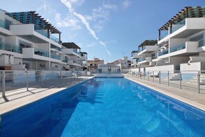 Un hotel moderno con piscina central, varios balcones y cielo despejado.