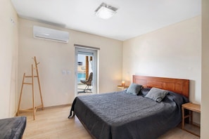 Un dormitorio con cama, mesita de noche, lámpara, escalera de madera y unidad de aire acondicionado.