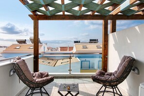 Un balcon avec deux fauteuils en osier, une petite table et une vue sur la mer et les bâtiments.