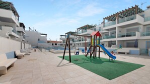 Une aire de jeux avec des balançoires et des toboggans, une moquette verte et un sol carrelé.
