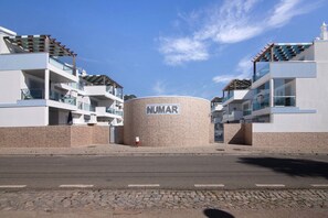 En moderne bygning med en cylindrisk midterstruktur med teksten 'NUMAR', altaner og en klar himmel.
