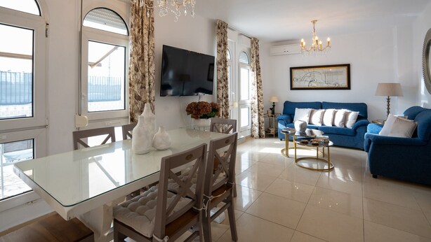 A modern living room with a blue sofa, a glass dining table, and a chandelier. - Refugio del Mar (Torre del Mar)