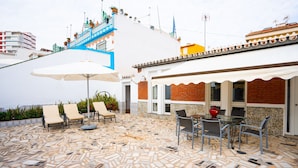 A patio with mosaic flooring, outdoor seating, and a staircase leading to a building with a white facade and blue accents. - Refugio del Mar (Torre del Mar)