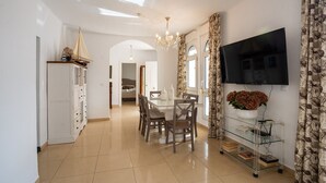 A spacious living area with a dining table, chairs, a chandelier, a television, and a bookshelf. - Refugio del Mar (Torre del Mar)