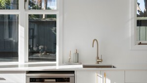 Una cocina con encimera blanca, pileta de acero inoxidable y ventana con vista a un patio trasero.