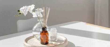 A table with a white tablecloth, a glass vase with white flowers, and a small bottle on a round tray.