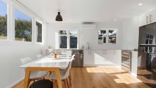 Una cocina moderna con armarios blancos, un lavavajillas de acero inoxidable y un horno. Hay una mesa de comedor con sillas y una lámpara colgante.