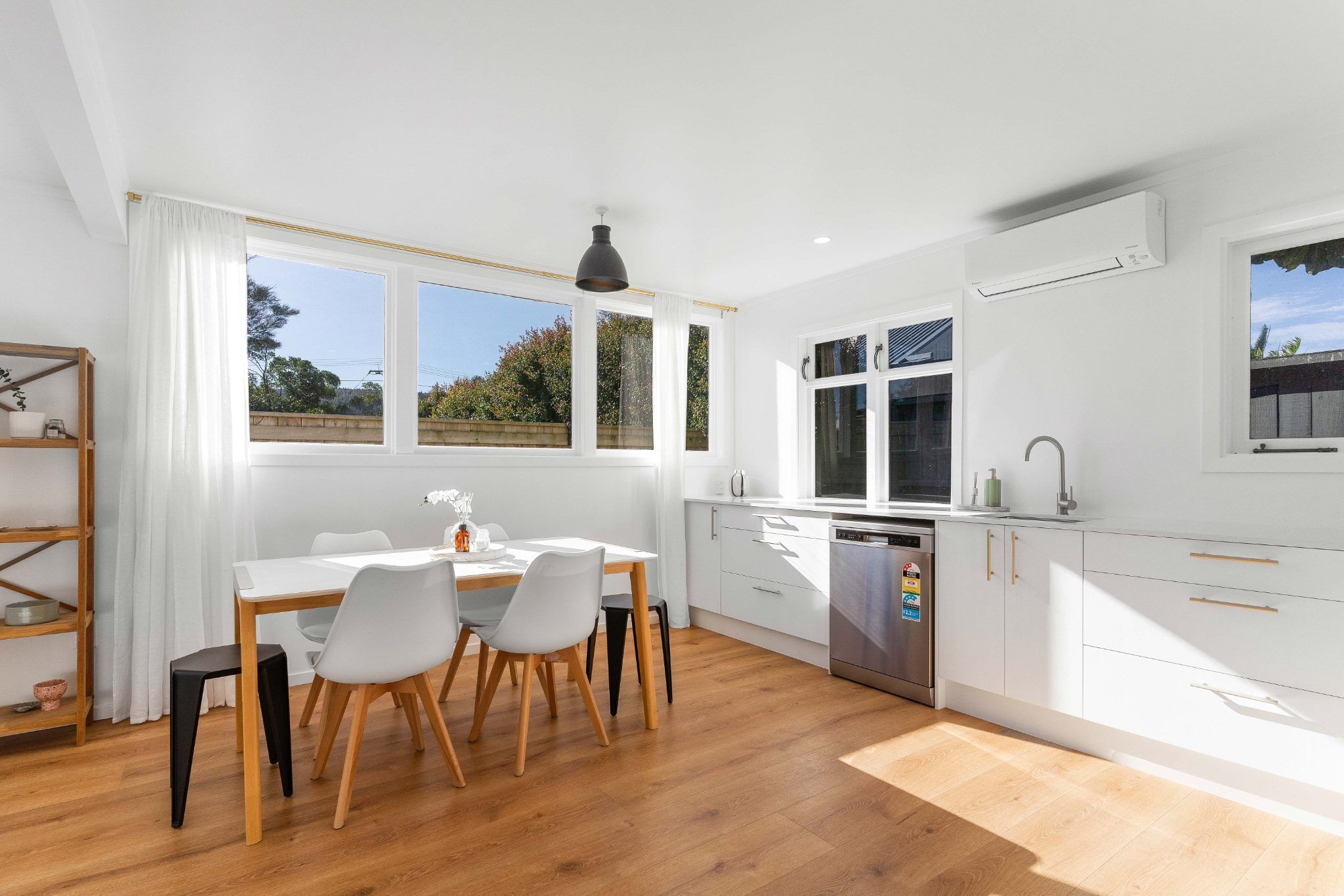 A modern kitchen with white cabinets, a wooden dining table, and a black pendant light.