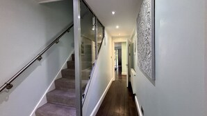 A hallway with a glass door leading to a staircase, a wooden floor, and a patterned wall.