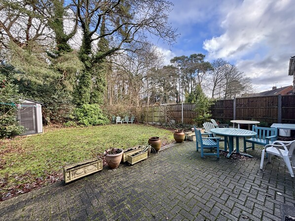A backyard with a brick patio, outdoor furniture, a small shed, and a variety of potted plants.