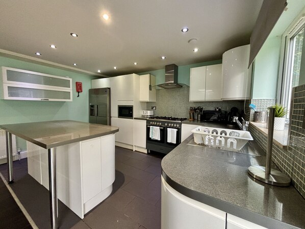 A modern kitchen with white cabinets, a stainless steel refrigerator, a stove, and a microwave.