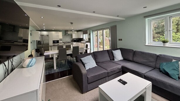 A modern kitchen with a dining area, a large grey sofa, and a white coffee table.