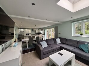 A modern kitchen with a dining area, a large grey sofa, and a white coffee table.