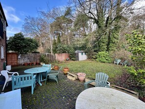 A patio with a table and chairs, surrounded by potted plants and a small shed.