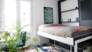 A bedroom with a bed, a window, a plant, and a wall-mounted shelf.