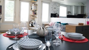 A dining area with a table set for four, a clock on the wall, and a kitchen in the background.