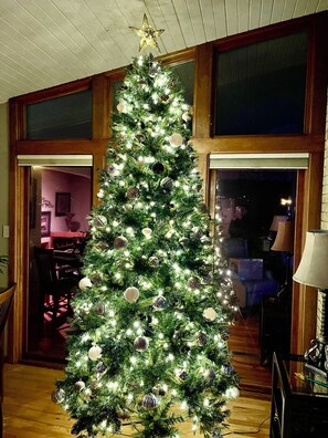 A Christmas tree with lights and ornaments in a room with wooden paneled walls and a window.