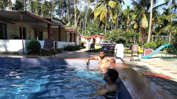 Una piscina con agua cristalina, rodeada de palmeras y una zona cubierta con sillas.