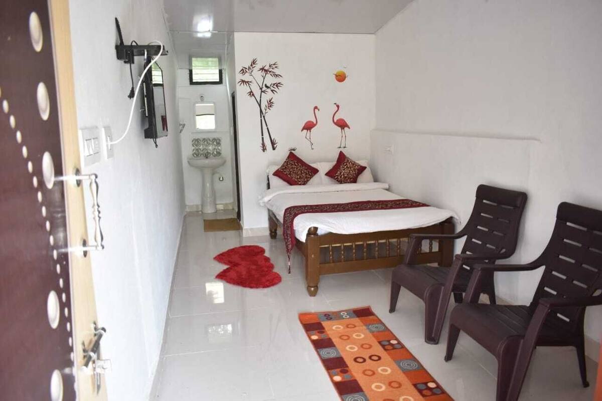 A bedroom with a bed, two chairs, a red rug, and wall art including flamingos and bamboo.