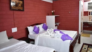 Habitación de hotel con dos camas, paredes de ladrillo rojo, ropa de cama blanca, almohadas moradas, un cuadro enmarcado en la pared y un mueble pequeño.