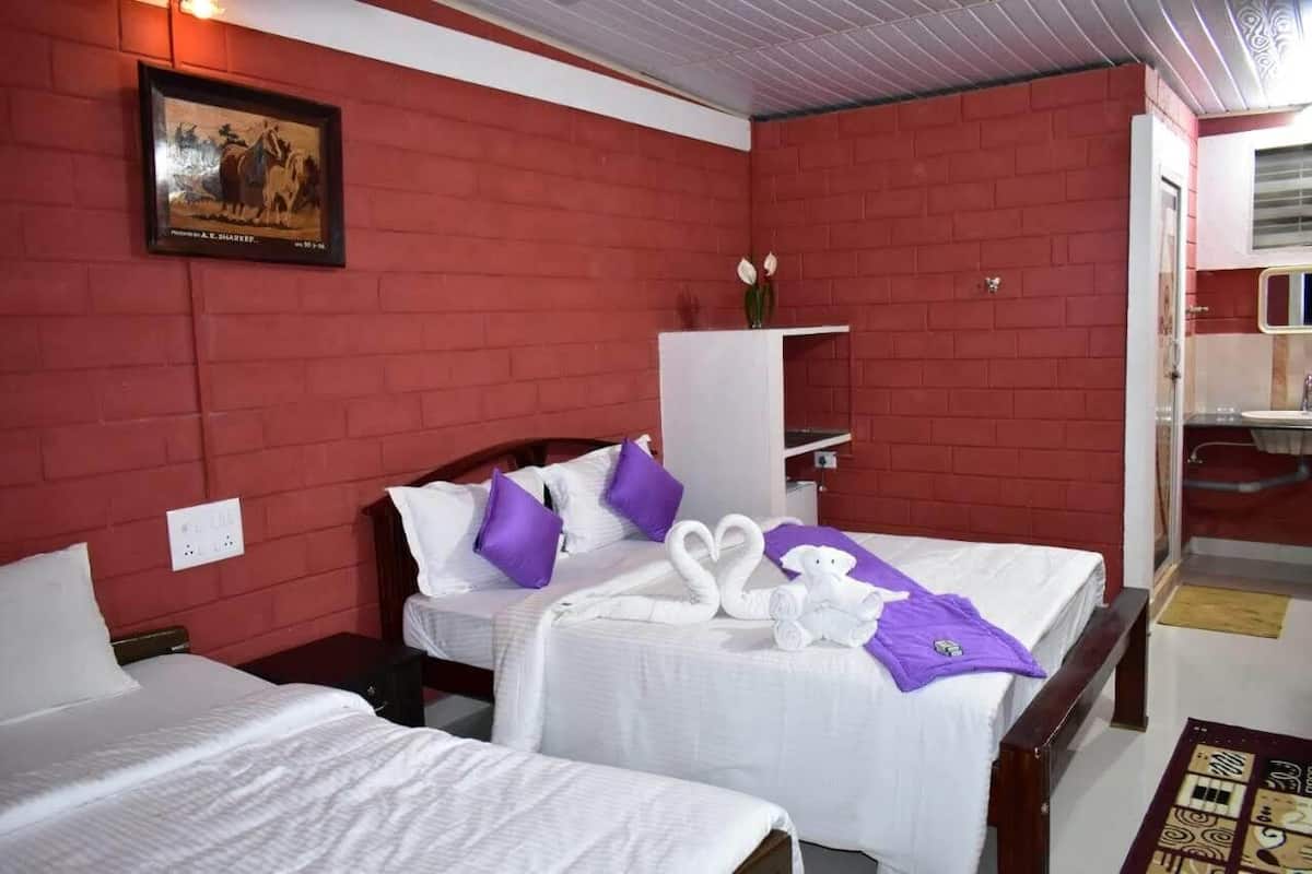 A hotel room with two beds, red brick walls, white bedding, purple pillows, a framed picture on the wall, and a small cabinet.