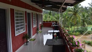 Un espacio al aire libre techado con un edificio rojo y blanco, plantas en macetas y vistas a palmeras.