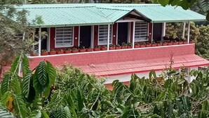 Un edificio con techo verde y paredes rojas, rodeado de abundante vegetación.