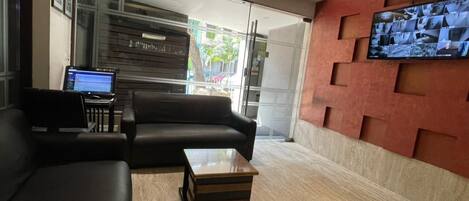 A modern lobby with a leather sofa, a wooden coffee table, and a flat-screen TV mounted on a red wall.