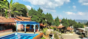A residential area with a swimming pool, a blue gazebo, and a view of the surrounding greenery and distant hills. - Nur Alam Hotel (Lembang)