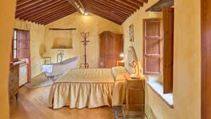 A bedroom with a wooden ceiling, a bed, a vanity, a bathtub, and a window.