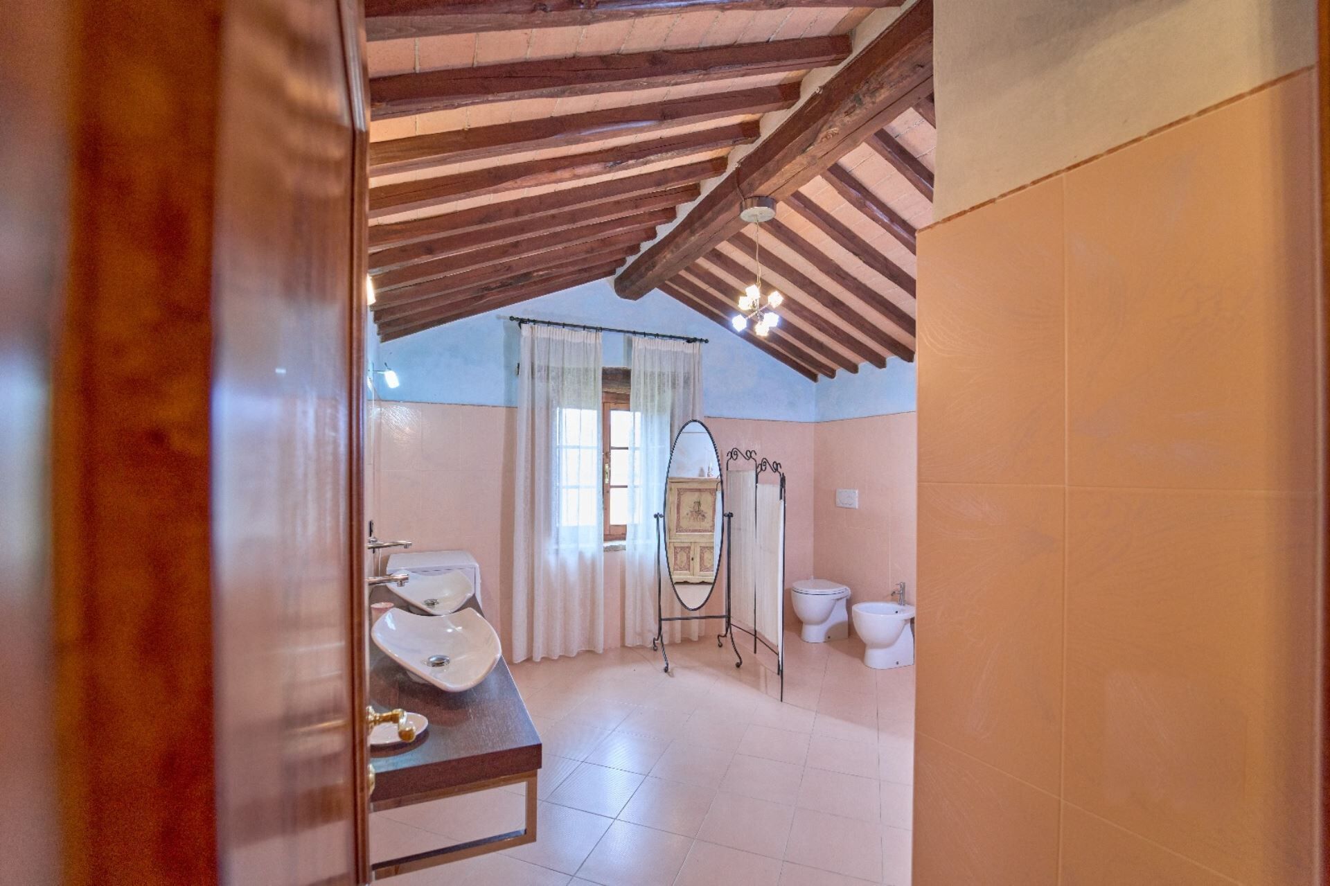 A bathroom with a wooden ceiling, a sink, a mirror, and two toilets.