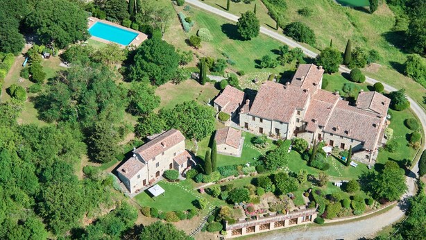 An aerial view of a property with a swimming pool, stone buildings, and well-maintained gardens.