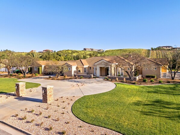 A residential area with a large house featuring a driveway, a lawn, and a hilly backdrop.