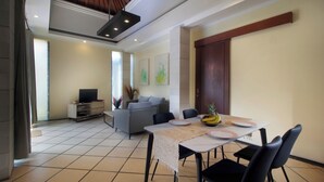A dining area with a table set for four, a sofa, and a television in the background. - Jayani Villa (Seminyak)